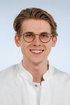Porträtfoto eines Mannes mit braunem Haar in weißem Arztkittel, der freundlich in die Kamera blickt