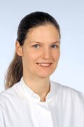 Porträtfoto einer Frau mit dunklen Haaren in einem weißen Arztkittel. Sie lächelt freundlich in die Kamera.