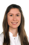 Porträtfoto einer Frau mit braunem Haar, die einen weißen Kittel trägt und freundlich in die Kamera schaut.