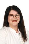 Porträtfoto einer Frau mit braunem Haar und runder Brille, die einen weißen Kittel trägt und freundlich in die Kamera schaut.
